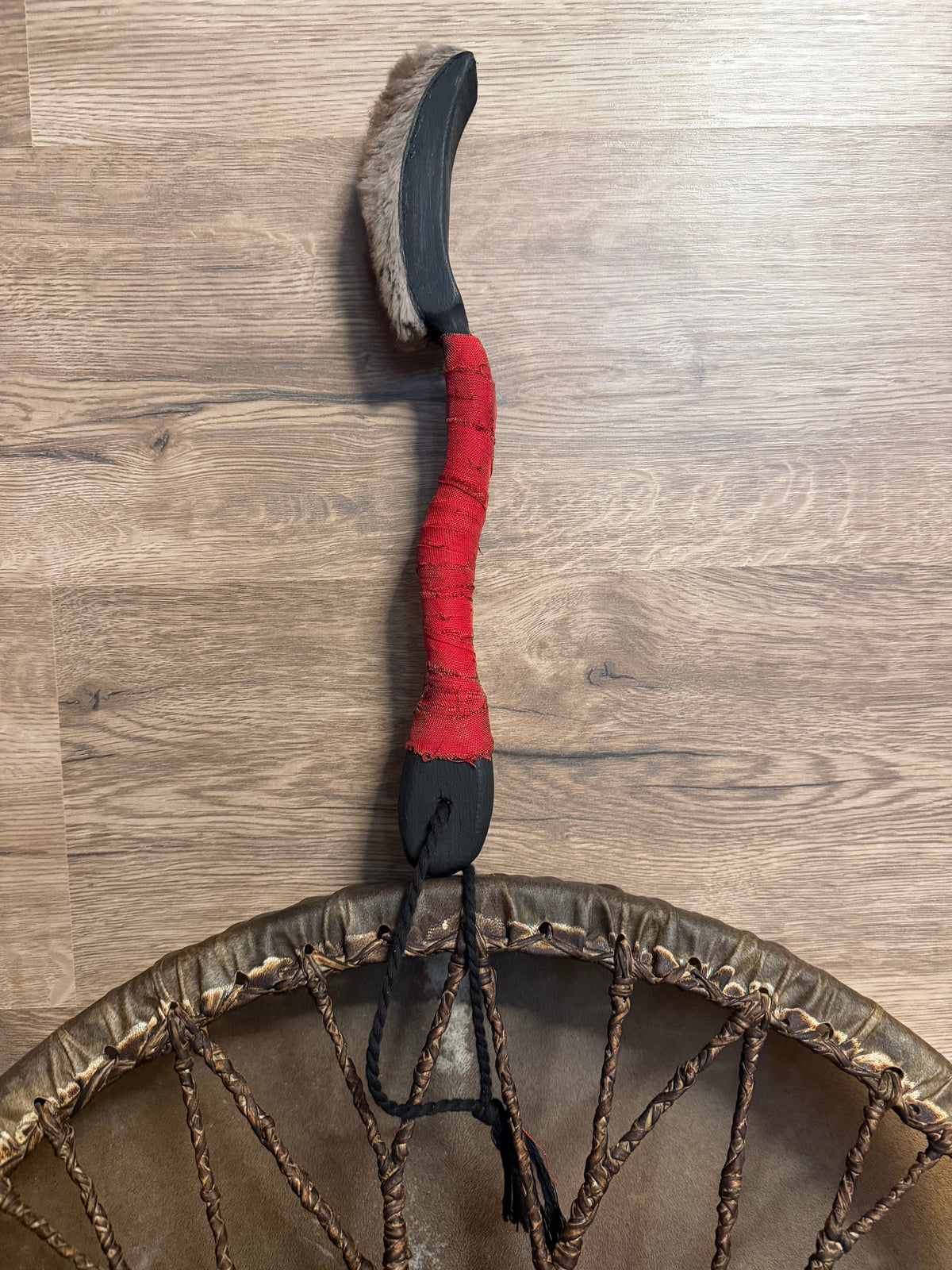 Shaman drum beater with red cord-wrapped grip beside a frame drum