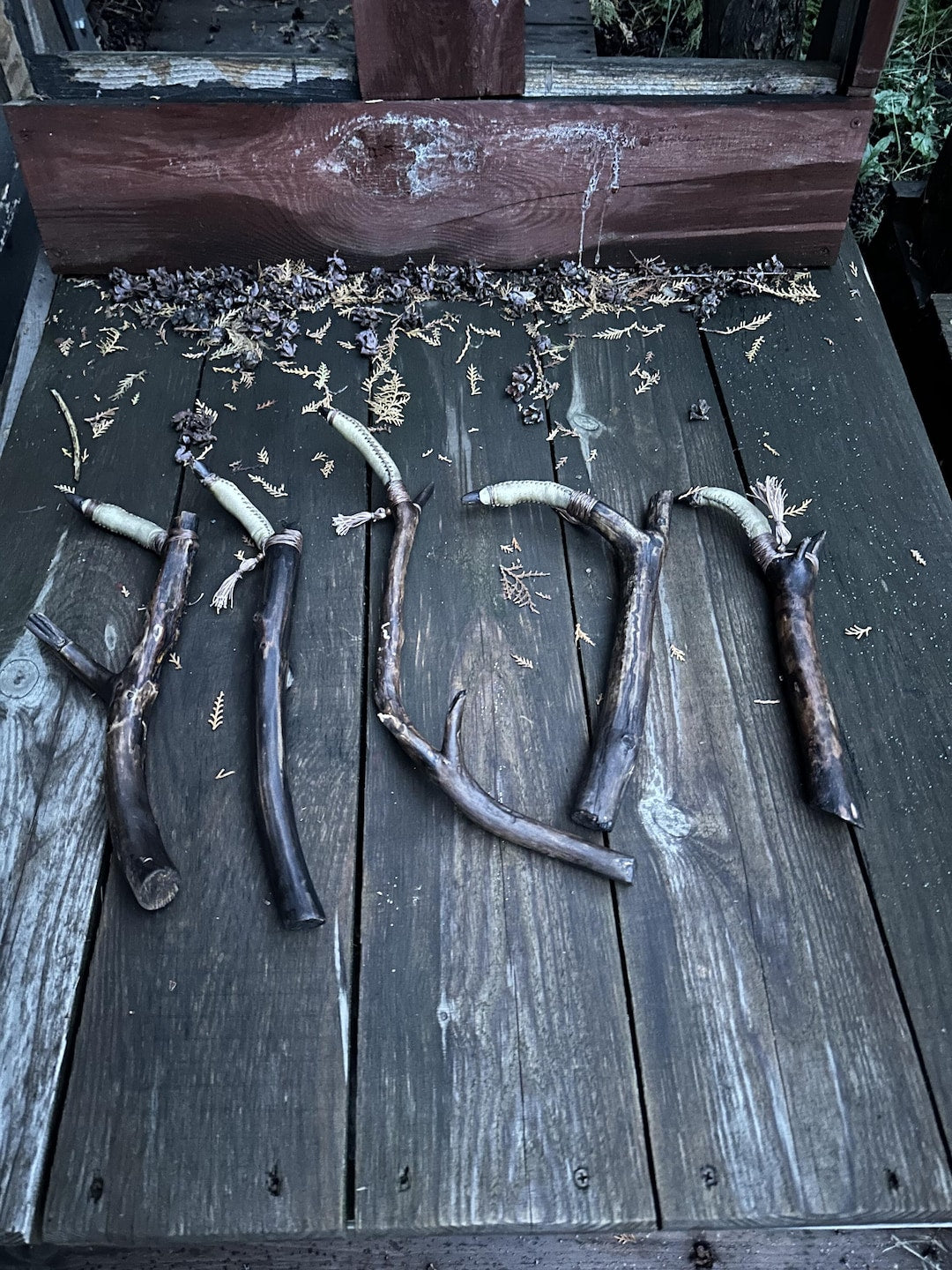 Several shaman's finger rattles laid out on dark wooden boards — pine branch handles with pale goat leather chambers