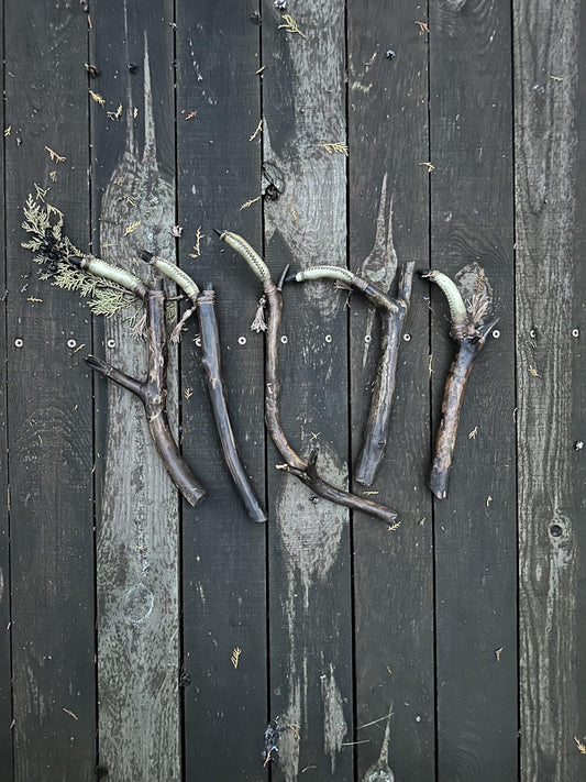 Five shaman's finger rattles on dark planks, each handle a different pine branch